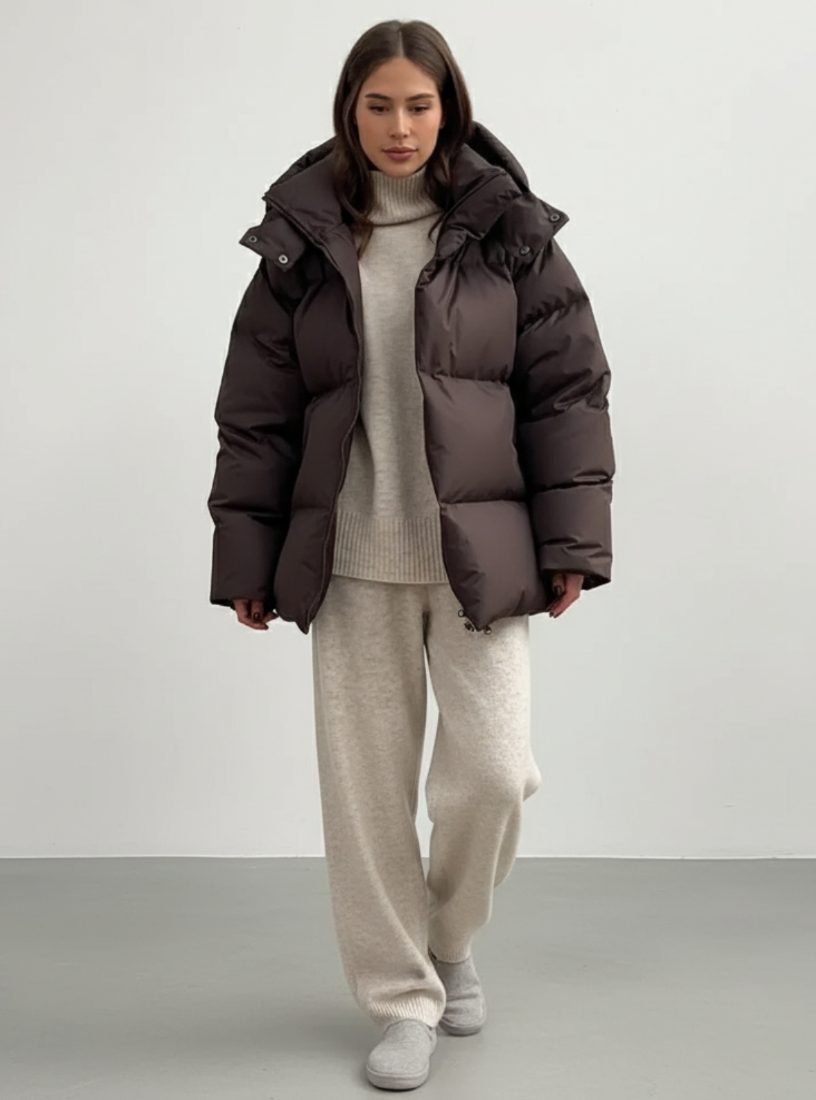 Person wearing a brown puffer jacket and beige outfit on a plain background