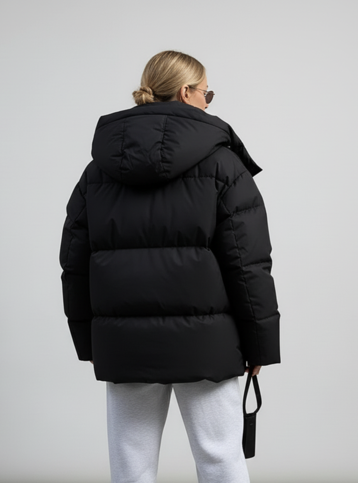 Person wearing a black puffer jacket and light gray pants against a plain background