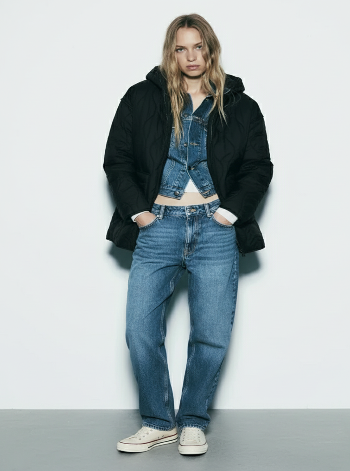 Person wearing a black coat, denim jacket, and jeans on a white background