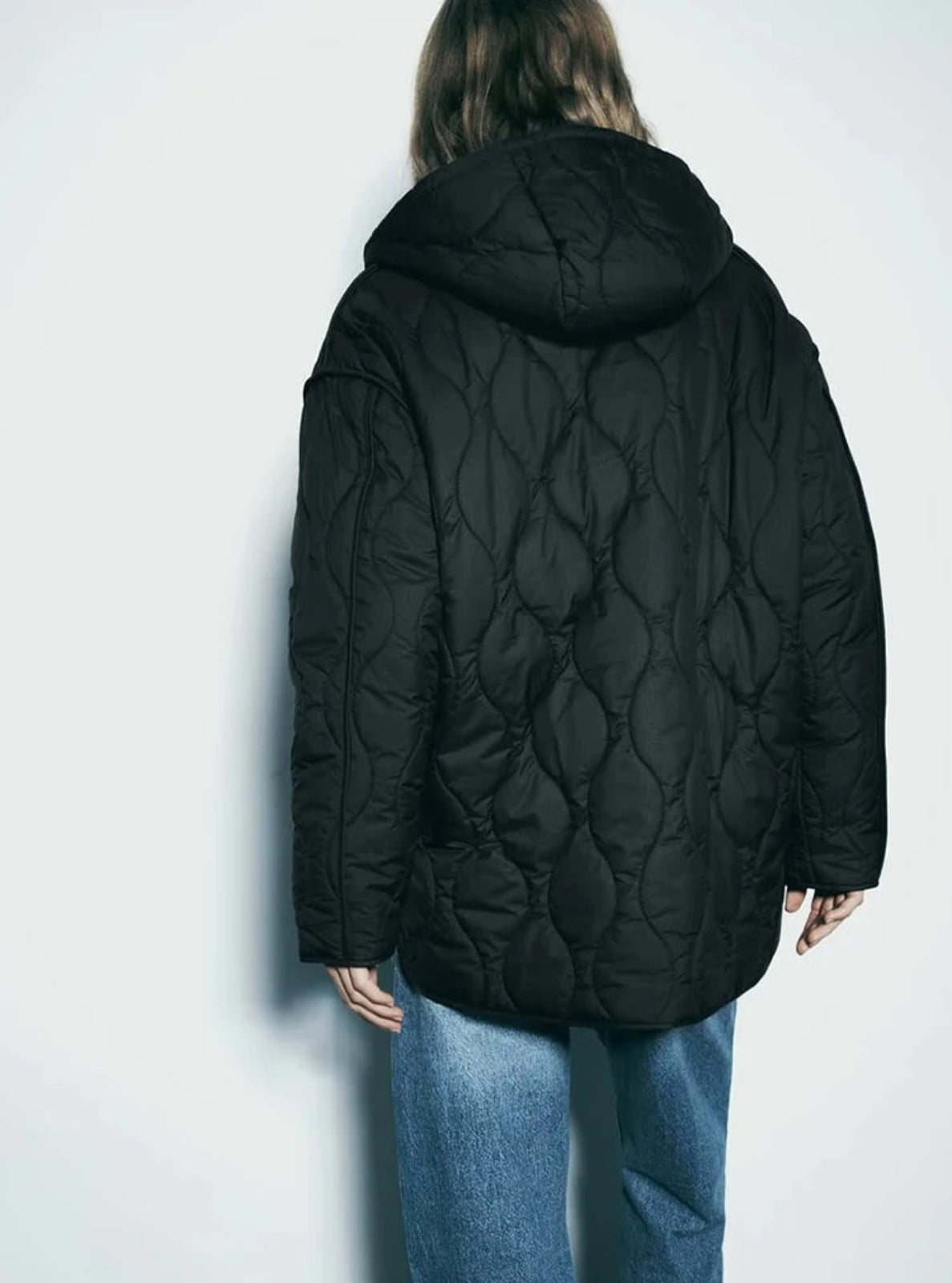 Person wearing a black quilted jacket against a white background