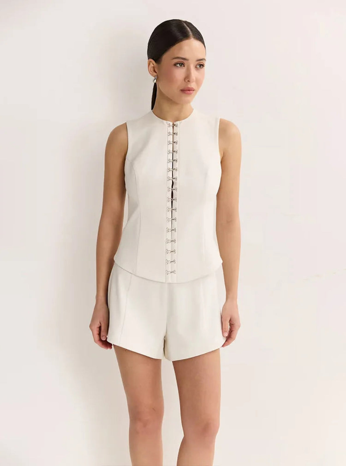Woman wearing a white sleeveless top and shorts set against a plain background