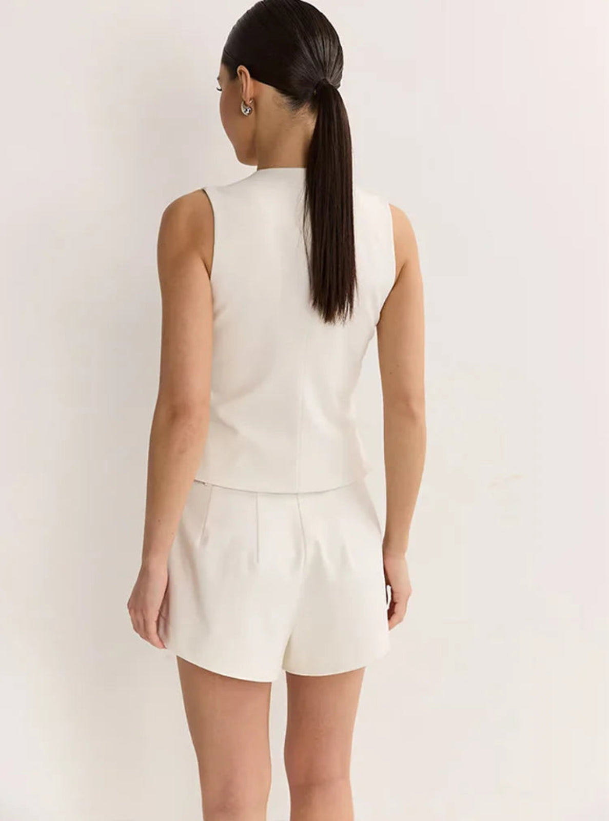 Woman wearing a white sleeveless top and shorts set against a plain background