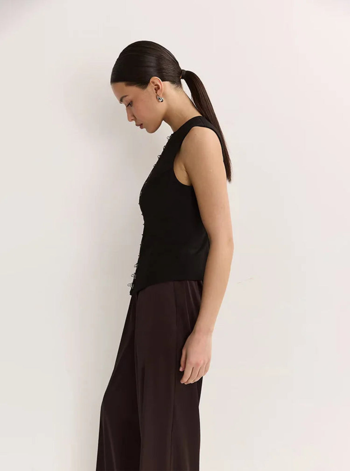 Woman wearing a black sleeveless top and dark pants against a white background