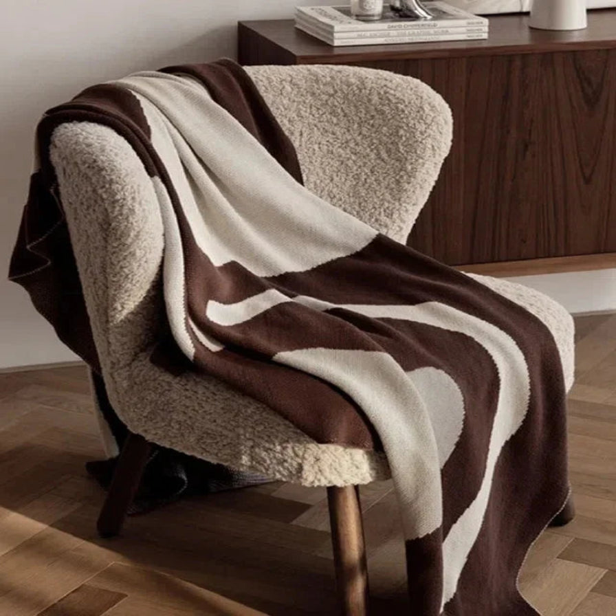 Brown and beige patterned blanket draped over a chair in a room with wooden flooring and furniture.