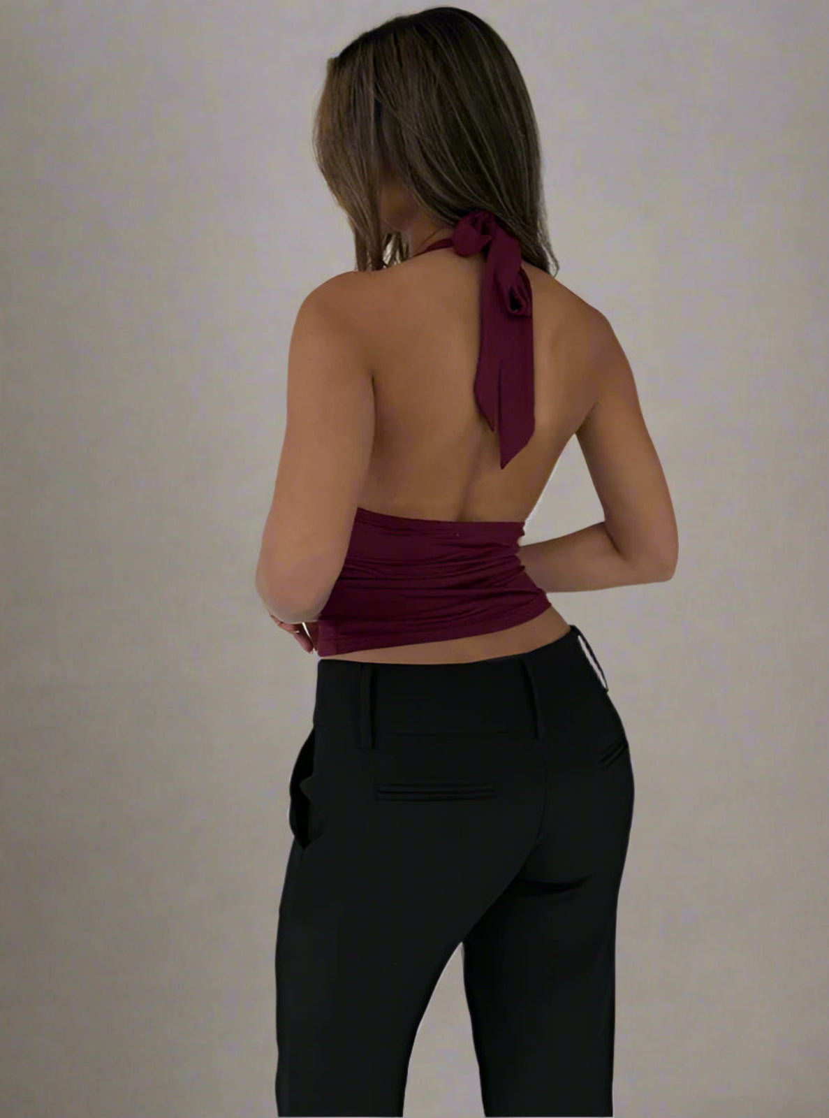 Person wearing a burgundy halter top with a tie detail and black pants on a plain background