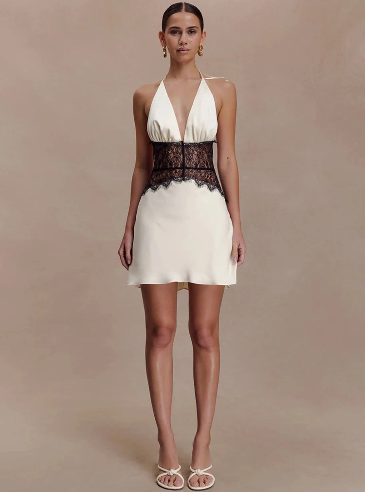 Woman wearing a white dress with black lace details on a beige background