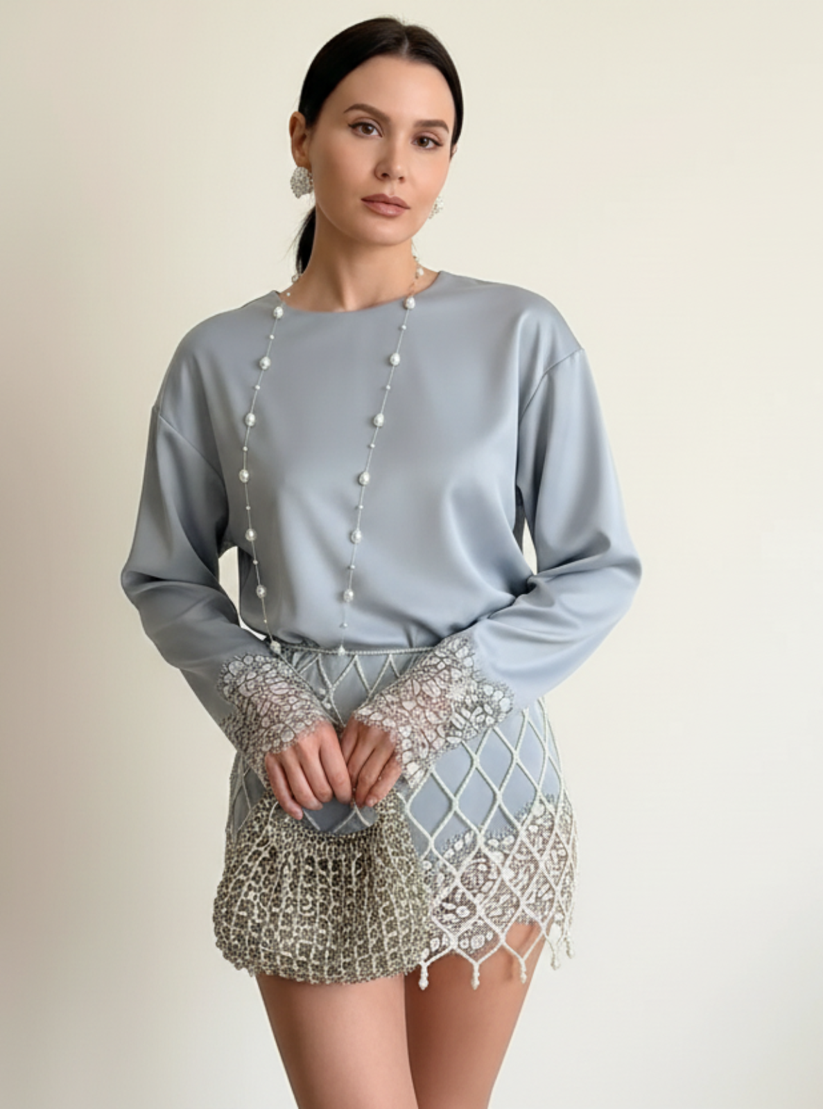Woman wearing a light blue top with pearl embellishments and a patterned skirt on a plain background