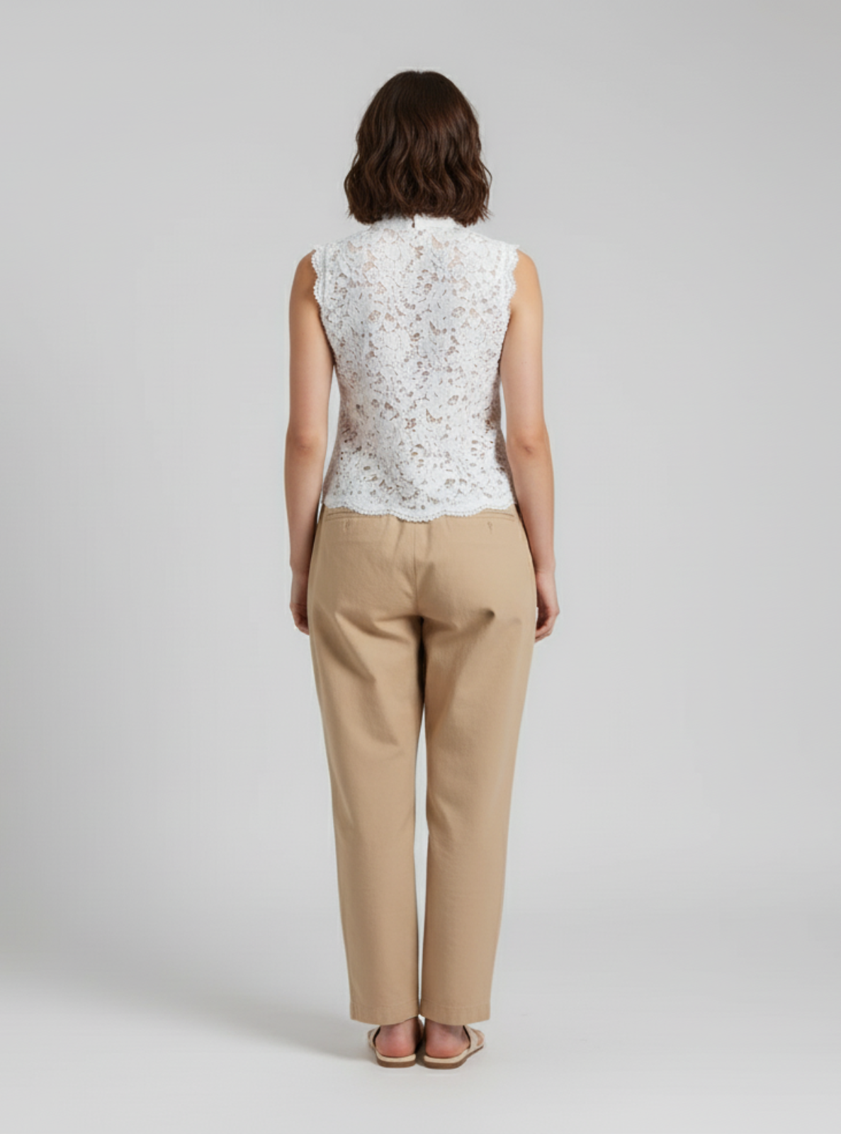 Woman wearing a white sleeveless top with floral pattern and beige pants on a gray background