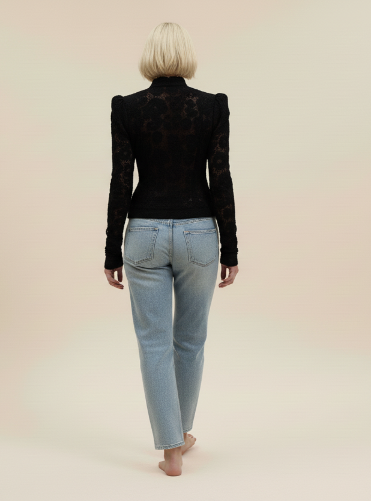 Person wearing a black jacket and light blue jeans on a beige background