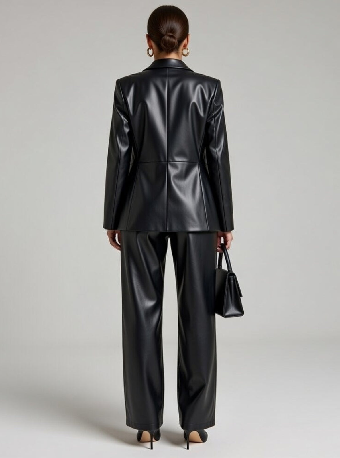 Person wearing a black leather suit holding a matching handbag against a neutral background