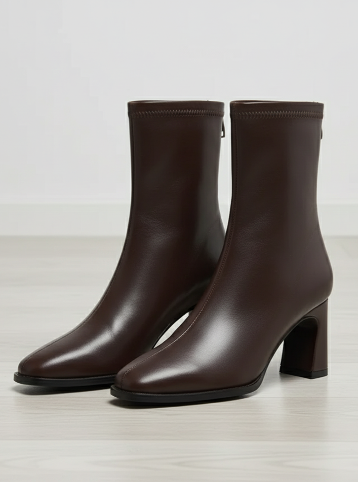 Pair of brown ankle boots on a light wooden floor with a neutral background