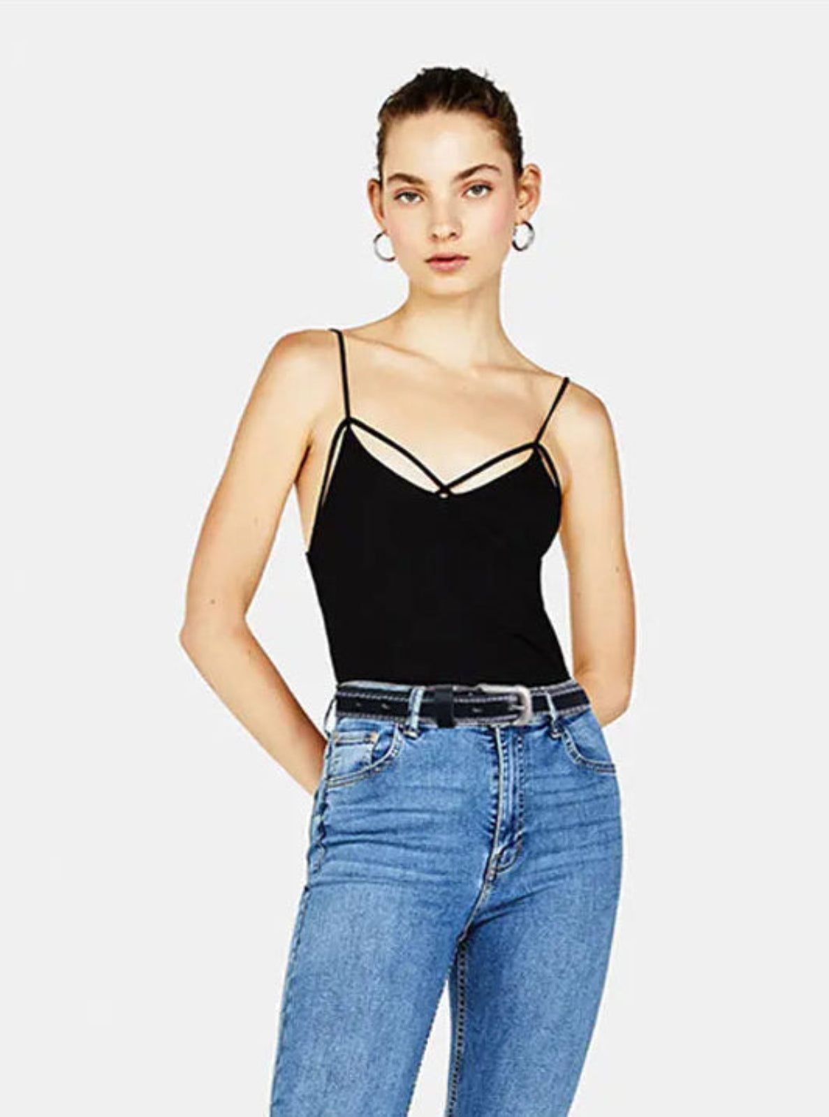 Woman wearing a black strappy top and blue jeans with black leather belt on a white background