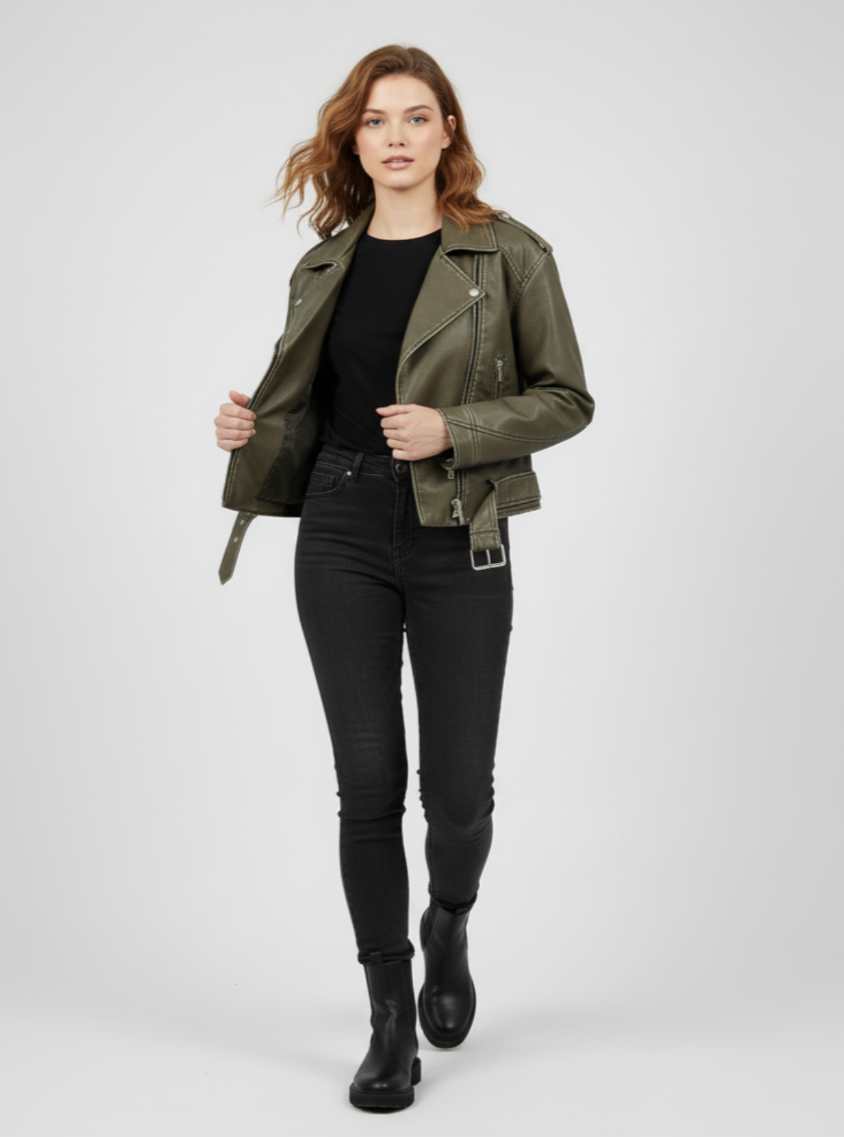 Woman wearing an olive green jacket, black top, and jeans on a white background