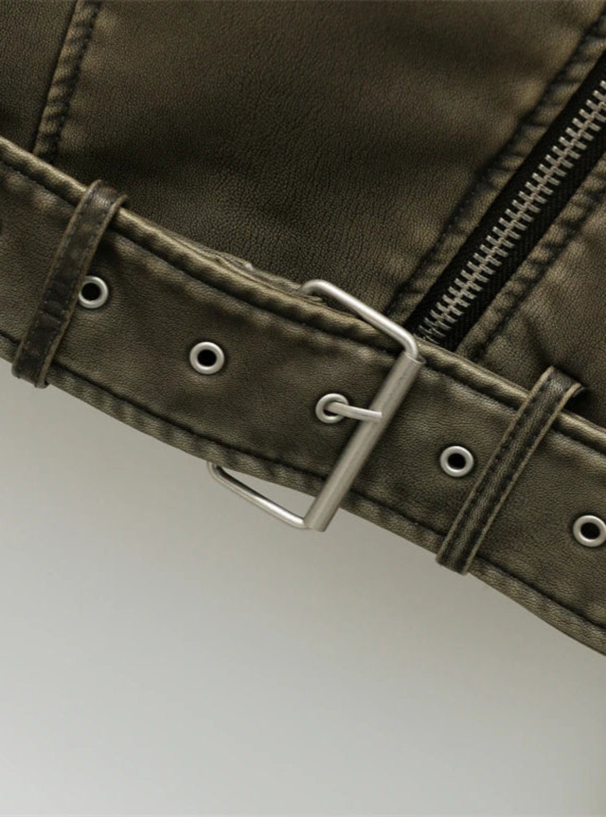 Close-up of a green jacket with a belt and zipper on a light gray background