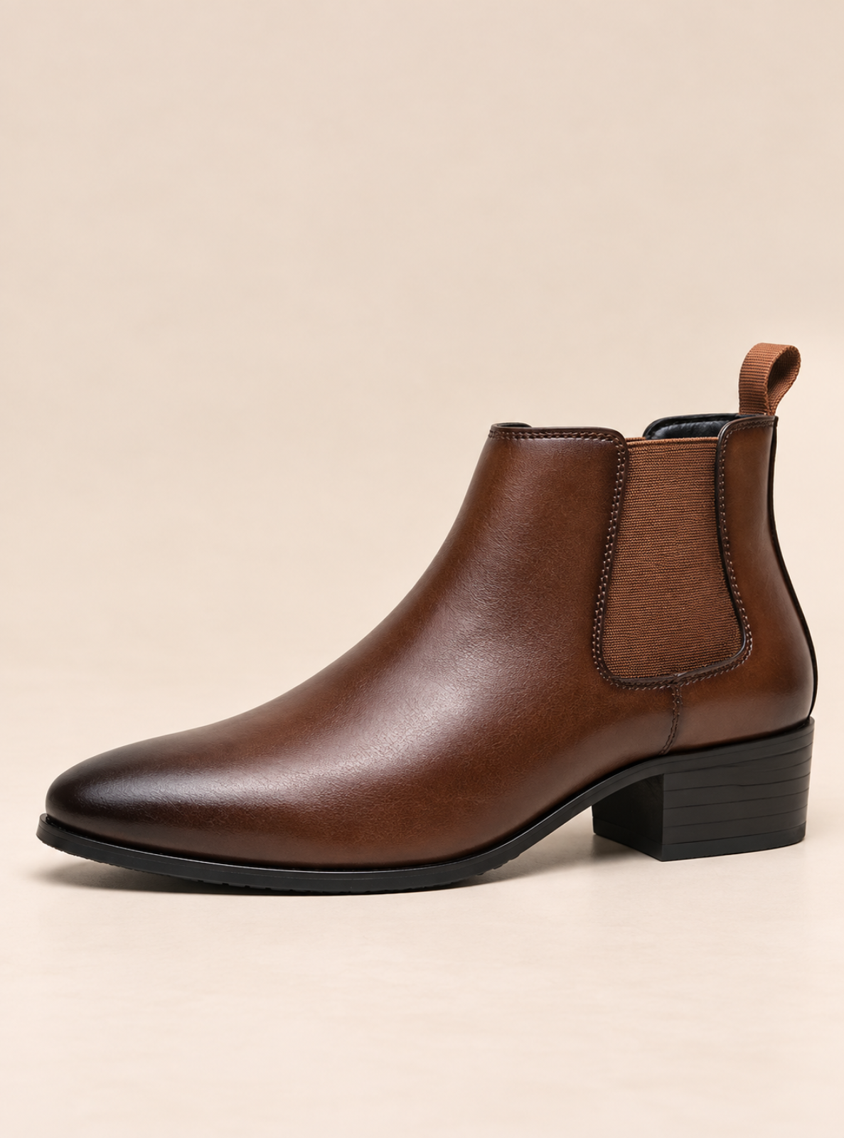 A brown leather Chelsea boot with a low block heel and black sole, shown from a side profile against a solid beige background.