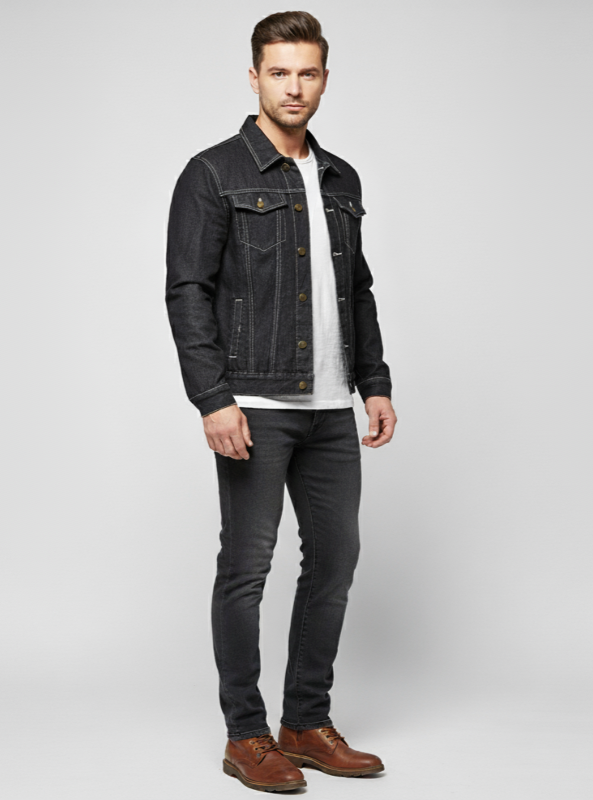 Man wearing a black denim jacket, white shirt, dark jeans, and brown shoes on a light gray background