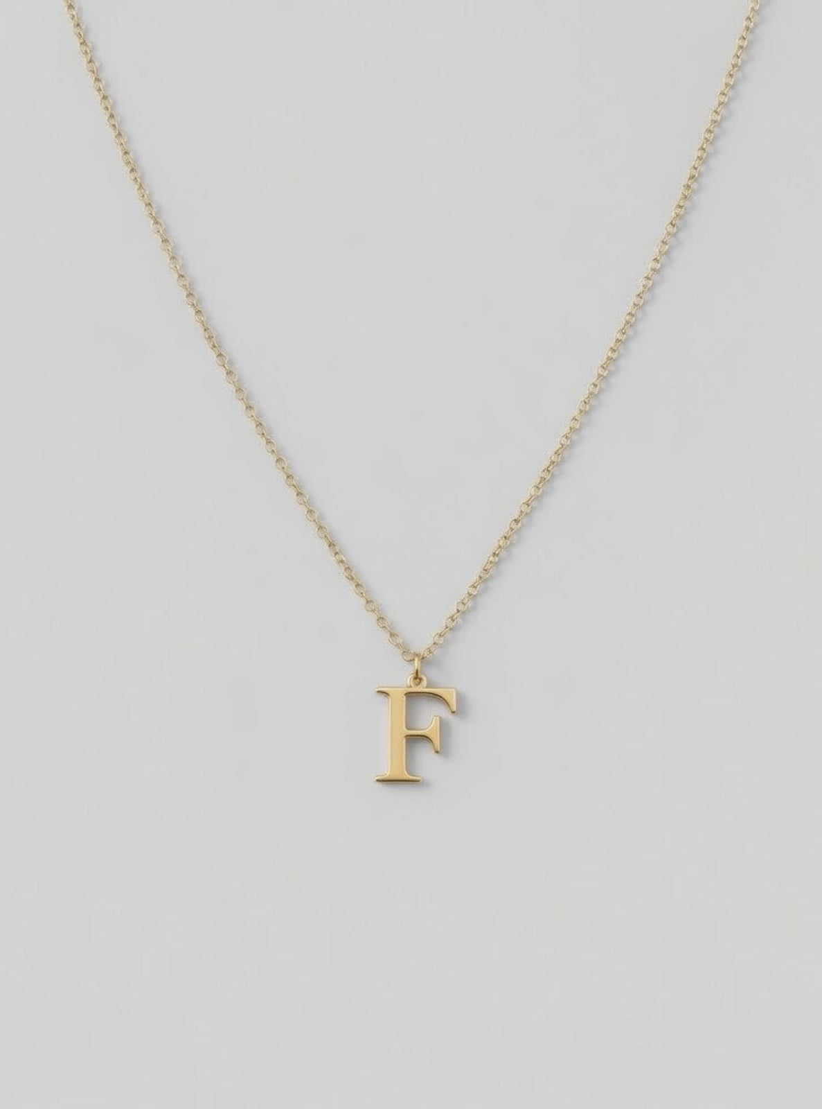 Gold necklace with a 'F' pendant on a light gray background