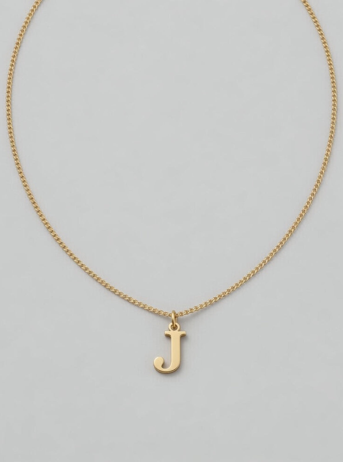 Gold necklace with a 'J' pendant on a gray background