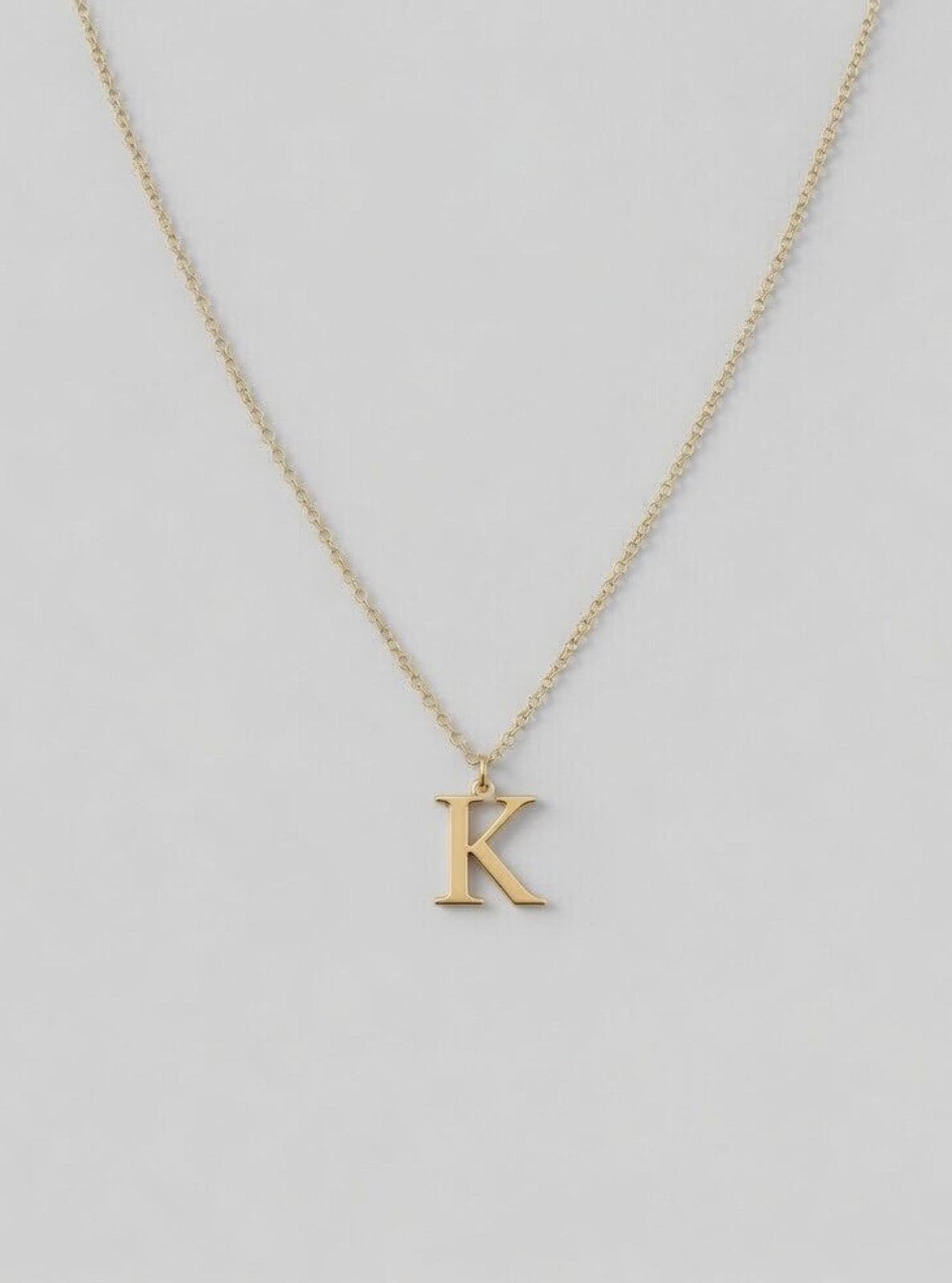 Gold necklace with a 'K' pendant on a light gray background