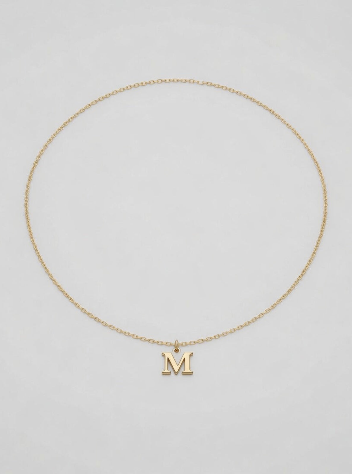 Gold necklace with a 'M' pendant on a light gray background