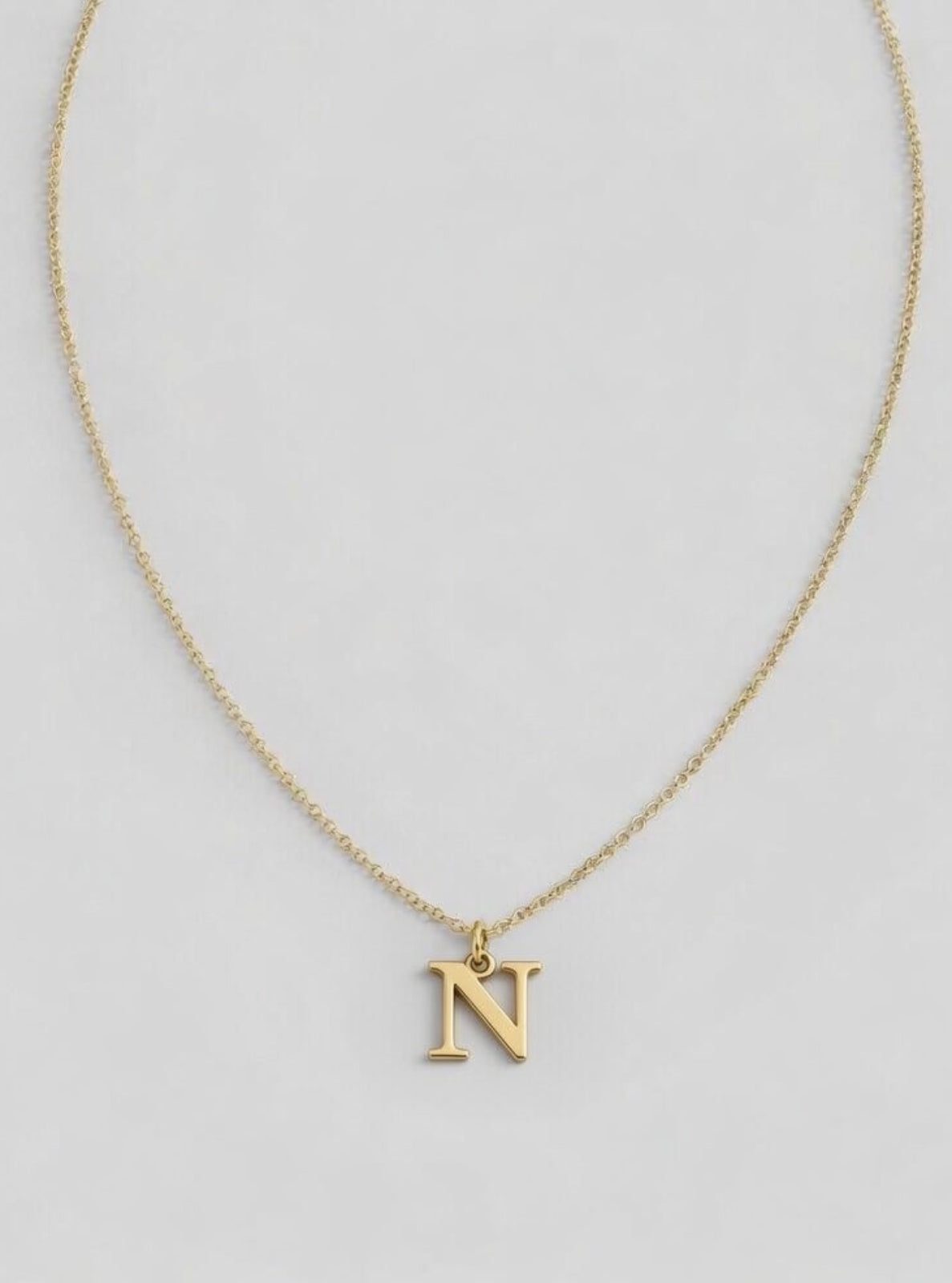 Gold necklace with a 'N' pendant on a light gray background