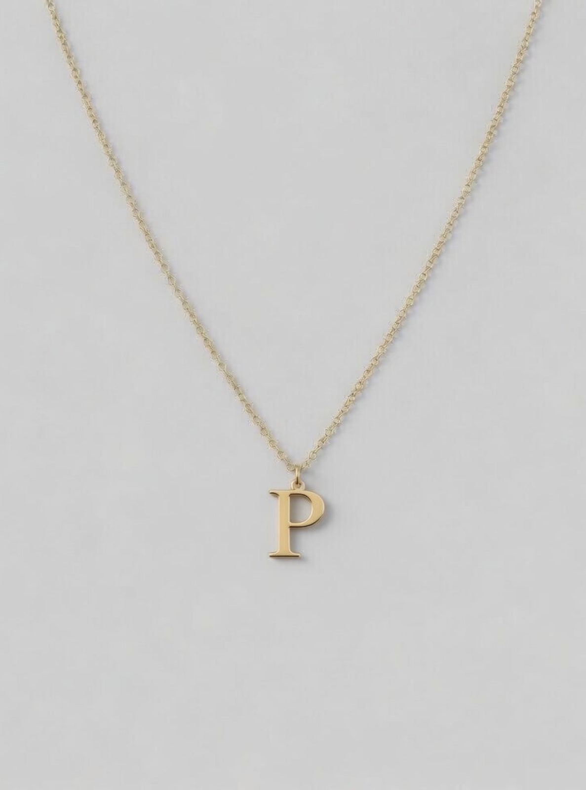 Gold necklace with a 'P' pendant on a light gray background