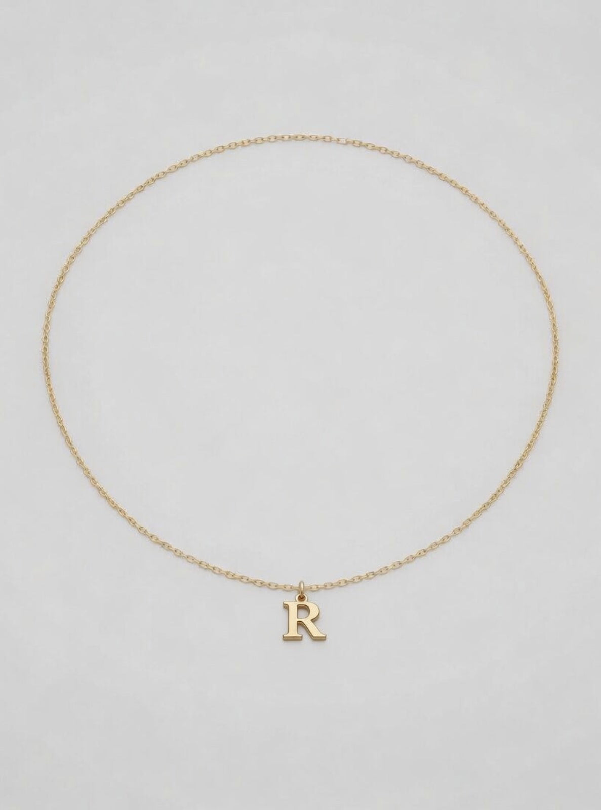 Gold necklace with a 'R' pendant on a light gray background
