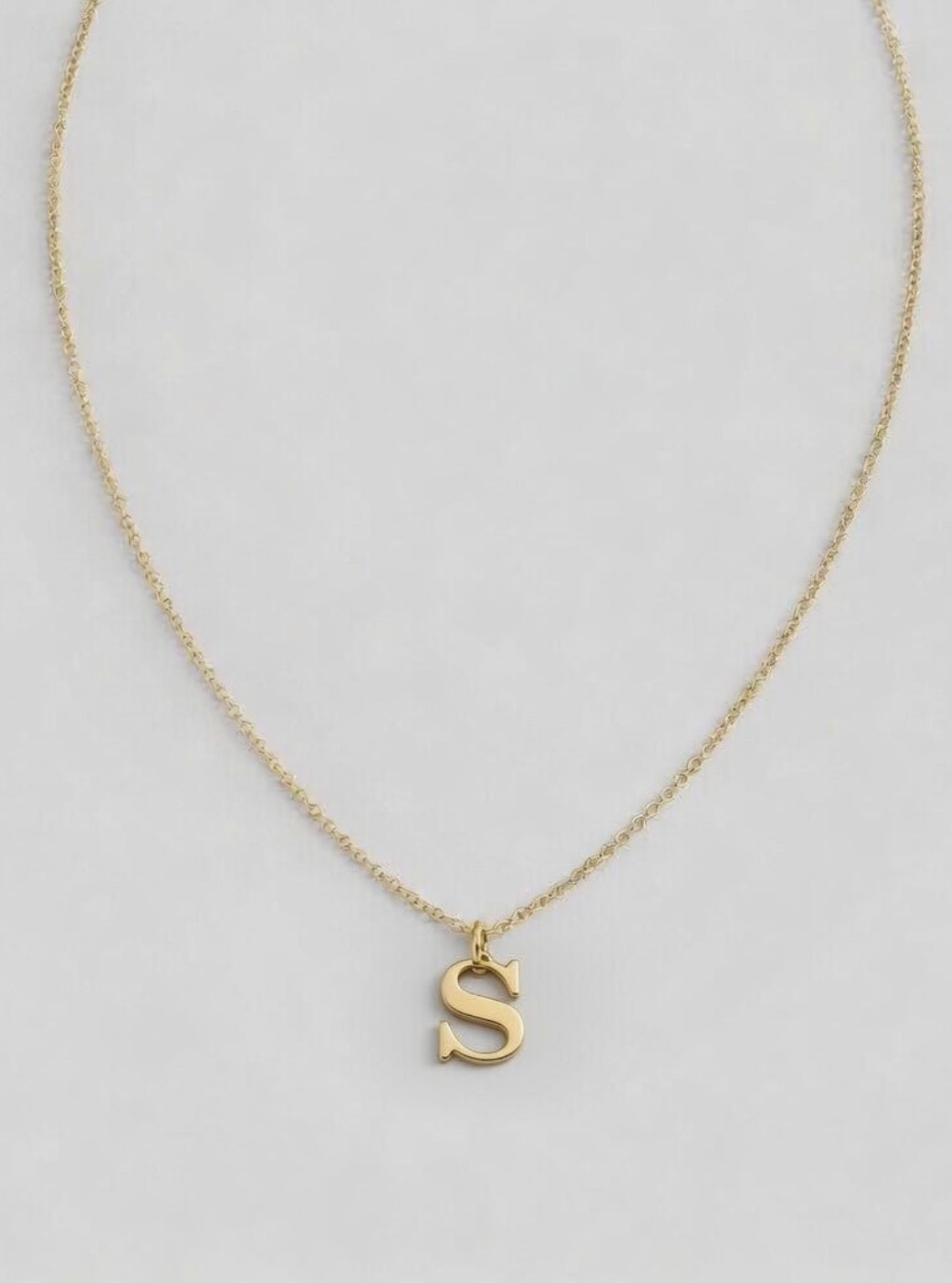 Gold necklace with a 'S' pendant on a light gray background