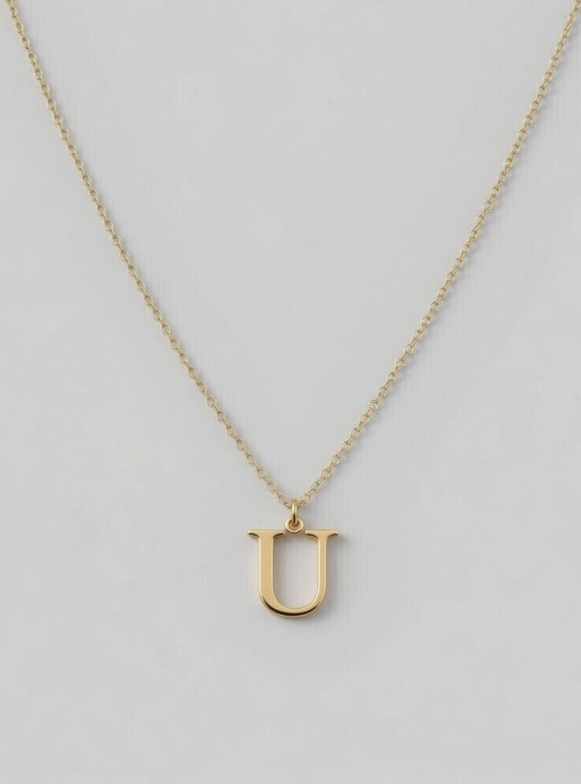 Gold necklace with a 'U' pendant on a light gray background