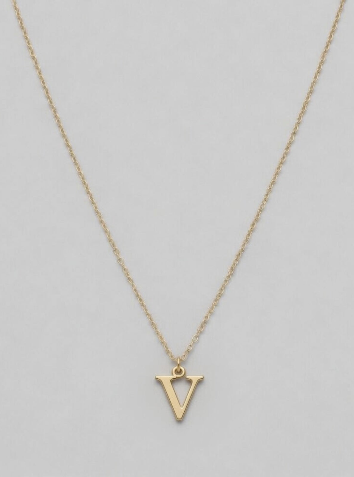 Gold necklace with a 'V' pendant on a light gray background