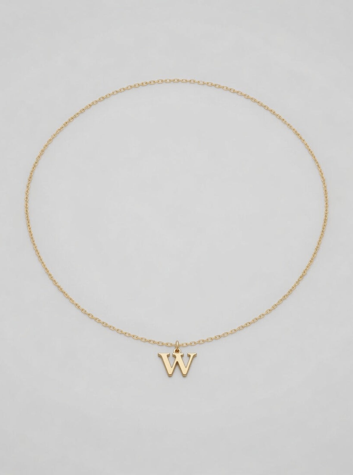 Gold necklace with a 'W' pendant on a light gray background
