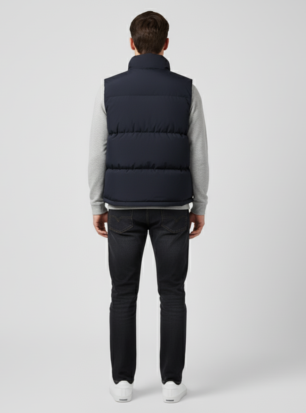 Man wearing a navy puffer vest over a light gray shirt on a white background