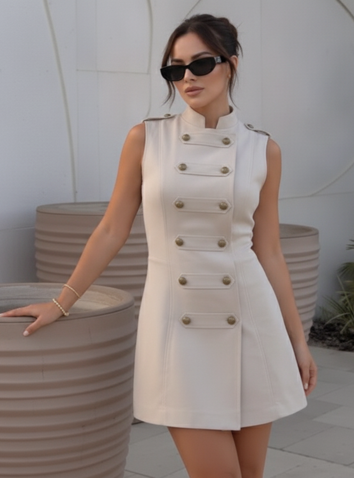 Woman in a white dress standing next to large planters against a white wall.