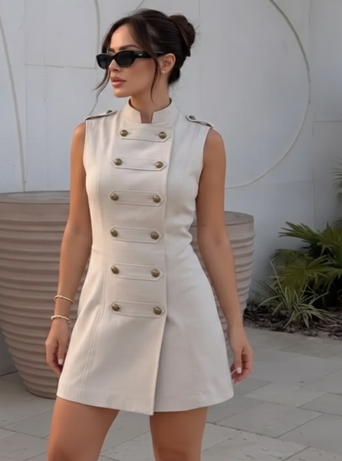 Woman wearing a white sleeveless dress with buttons in an outdoor setting.