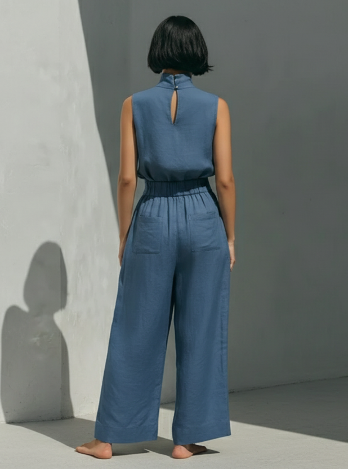 Person wearing a blue jumpsuit standing against a gray wall.