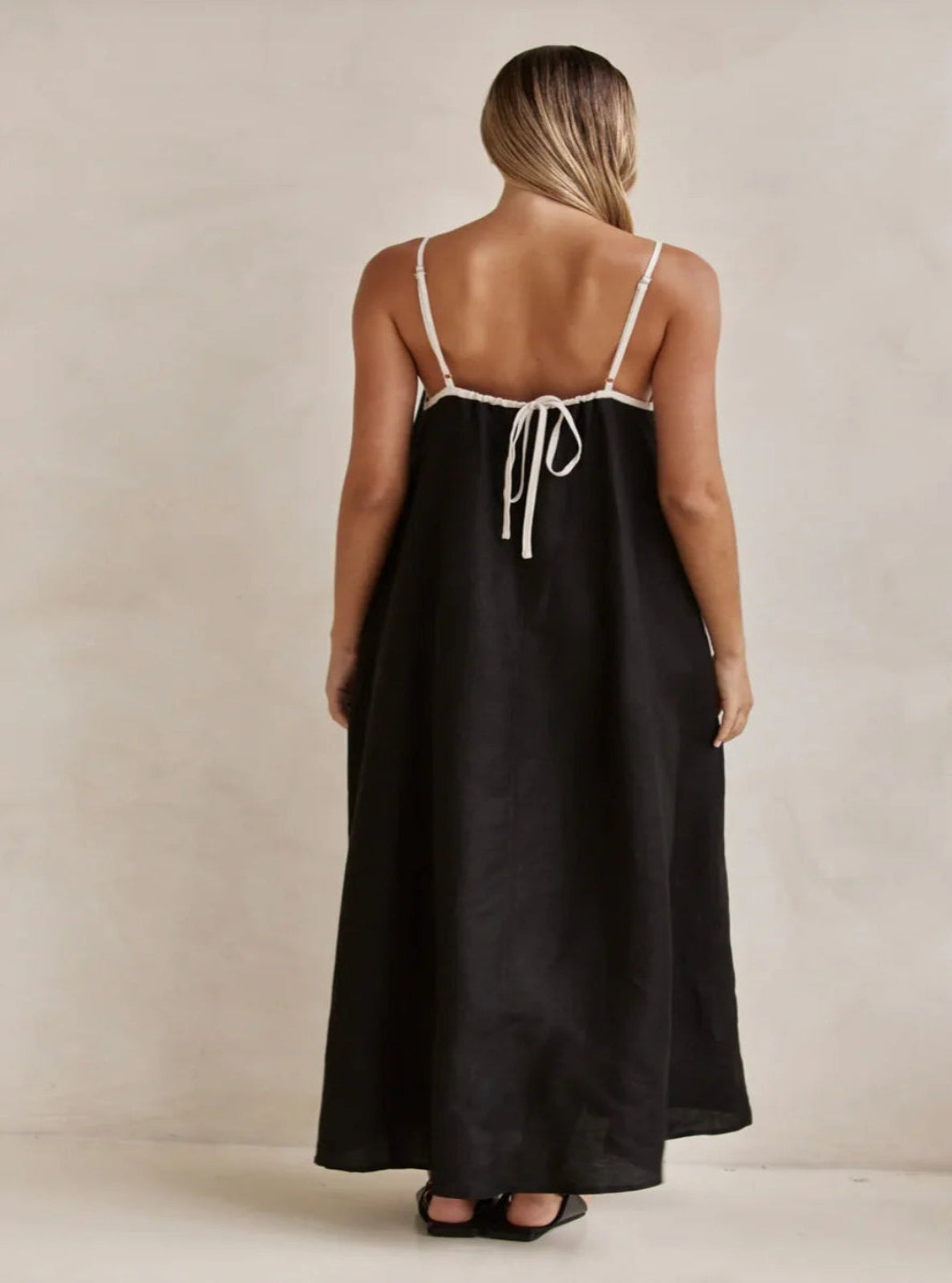 Woman wearing a black slip dress with thin straps against a beige background