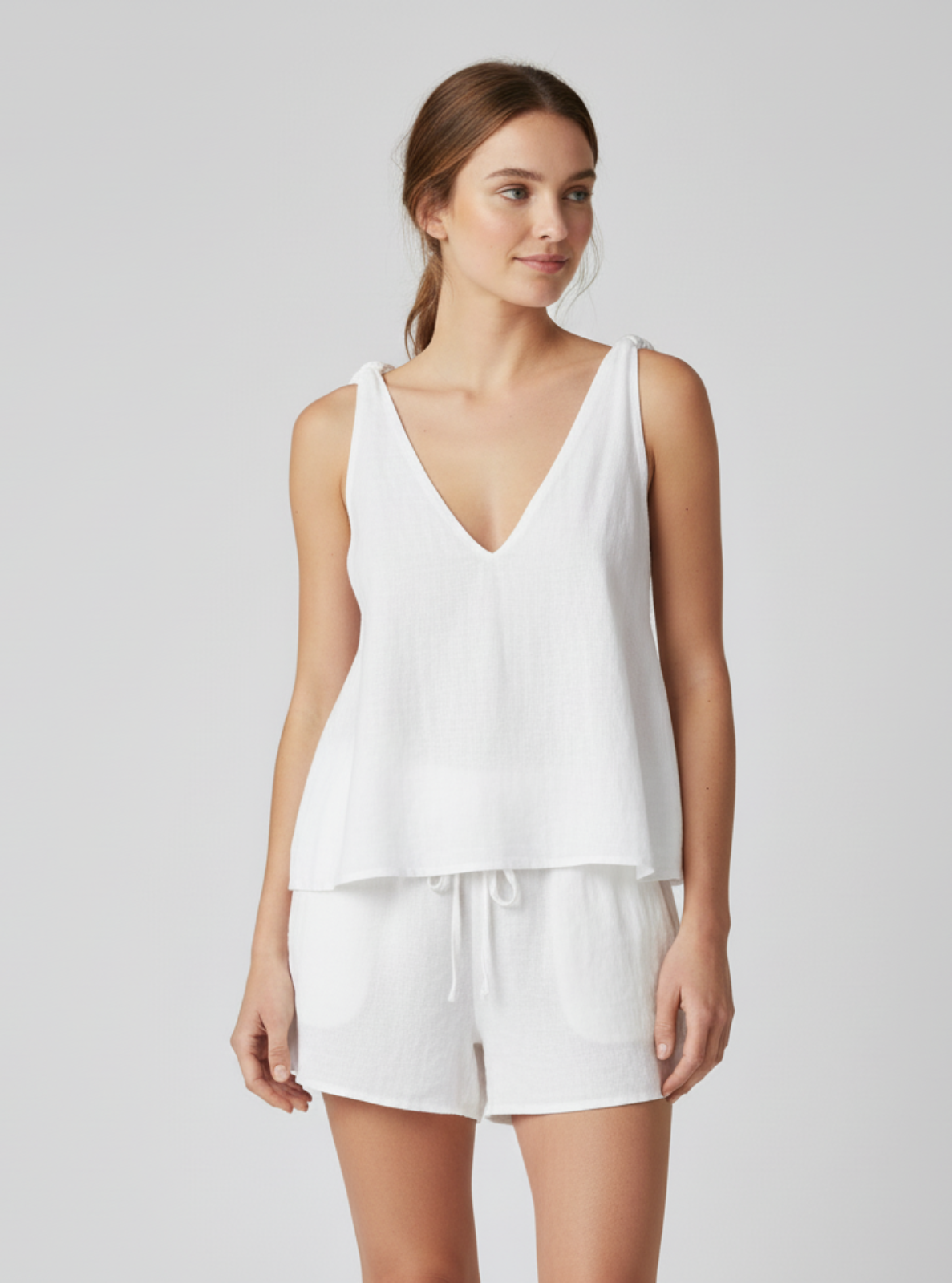 Woman wearing a white sleeveless top and shorts on a light gray background
