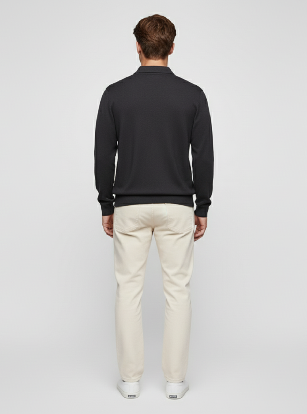 Man wearing a dark sweater and light pants on a white background