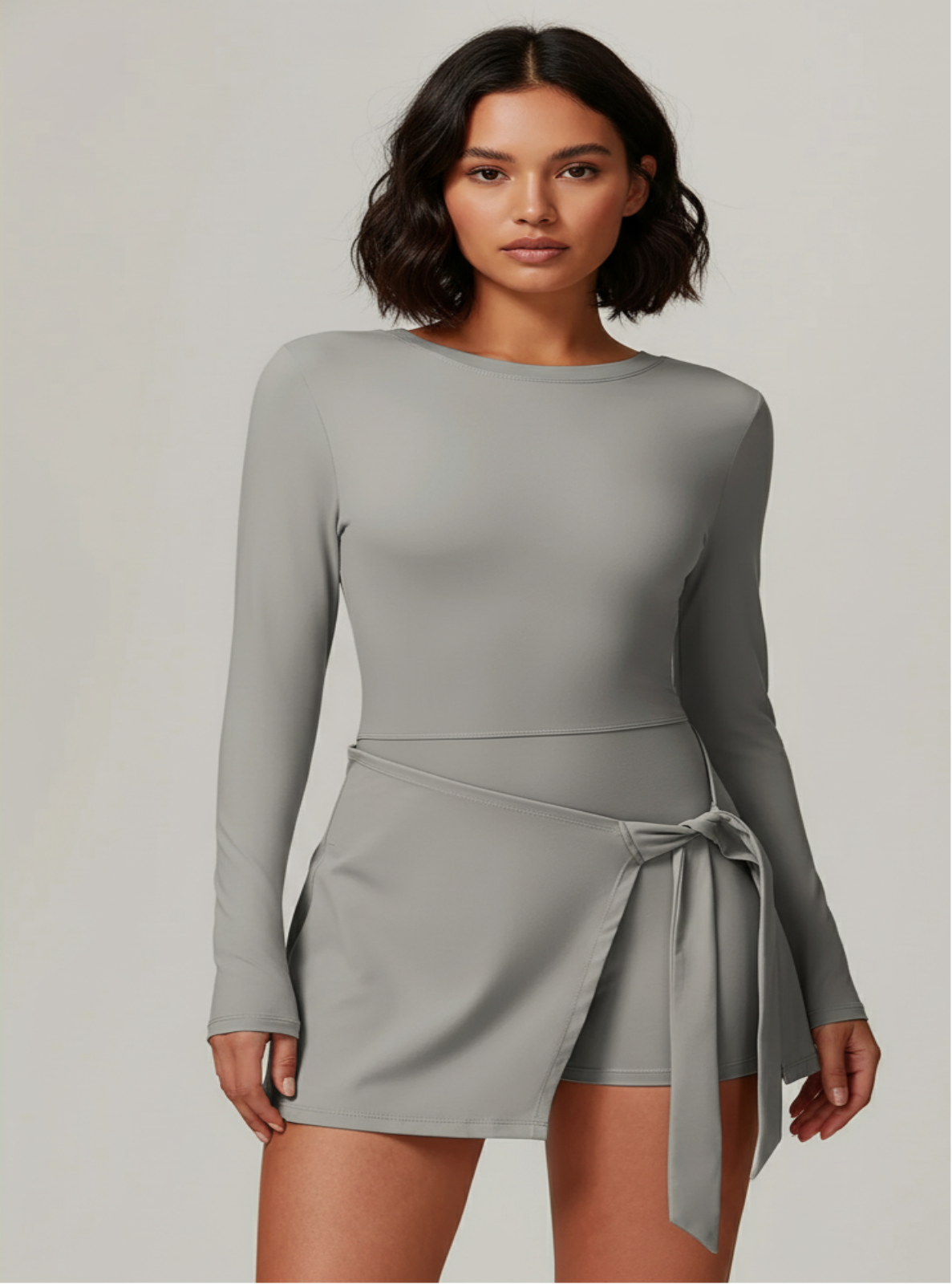 Woman wearing a gray long-sleeve dress with a belt on a plain background