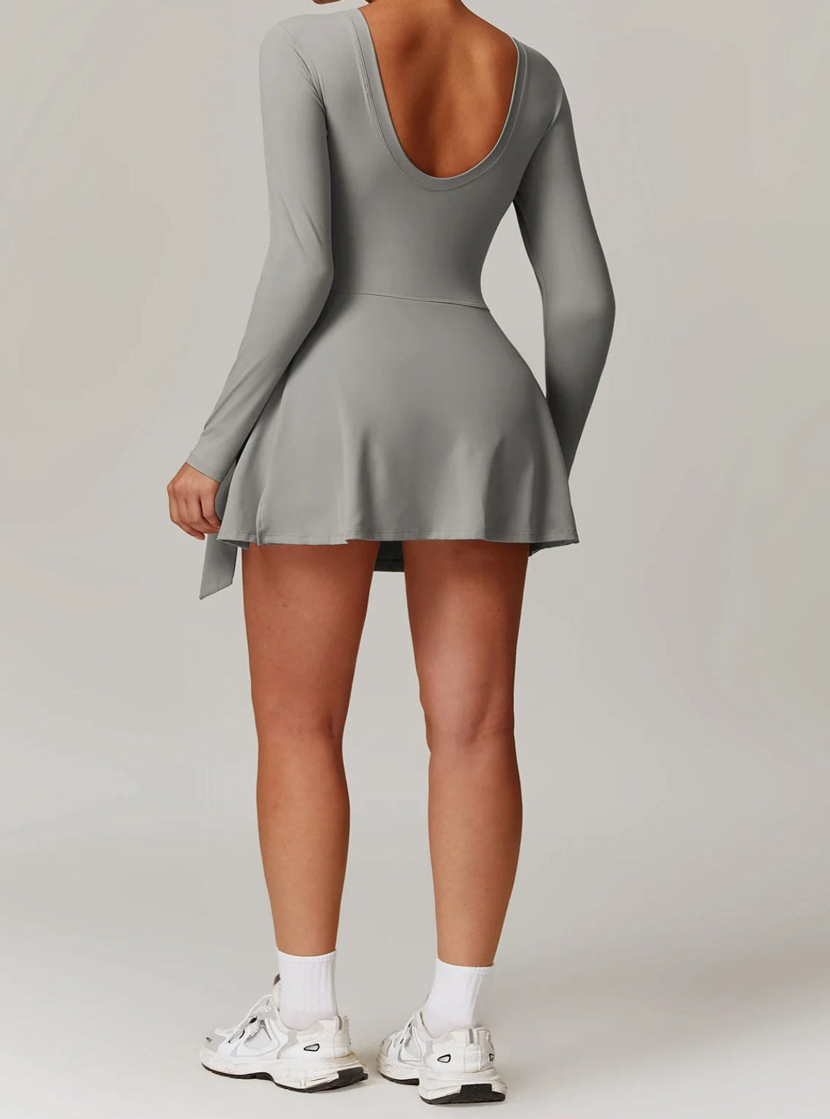 Person wearing a gray dress with long sleeves and a plain background