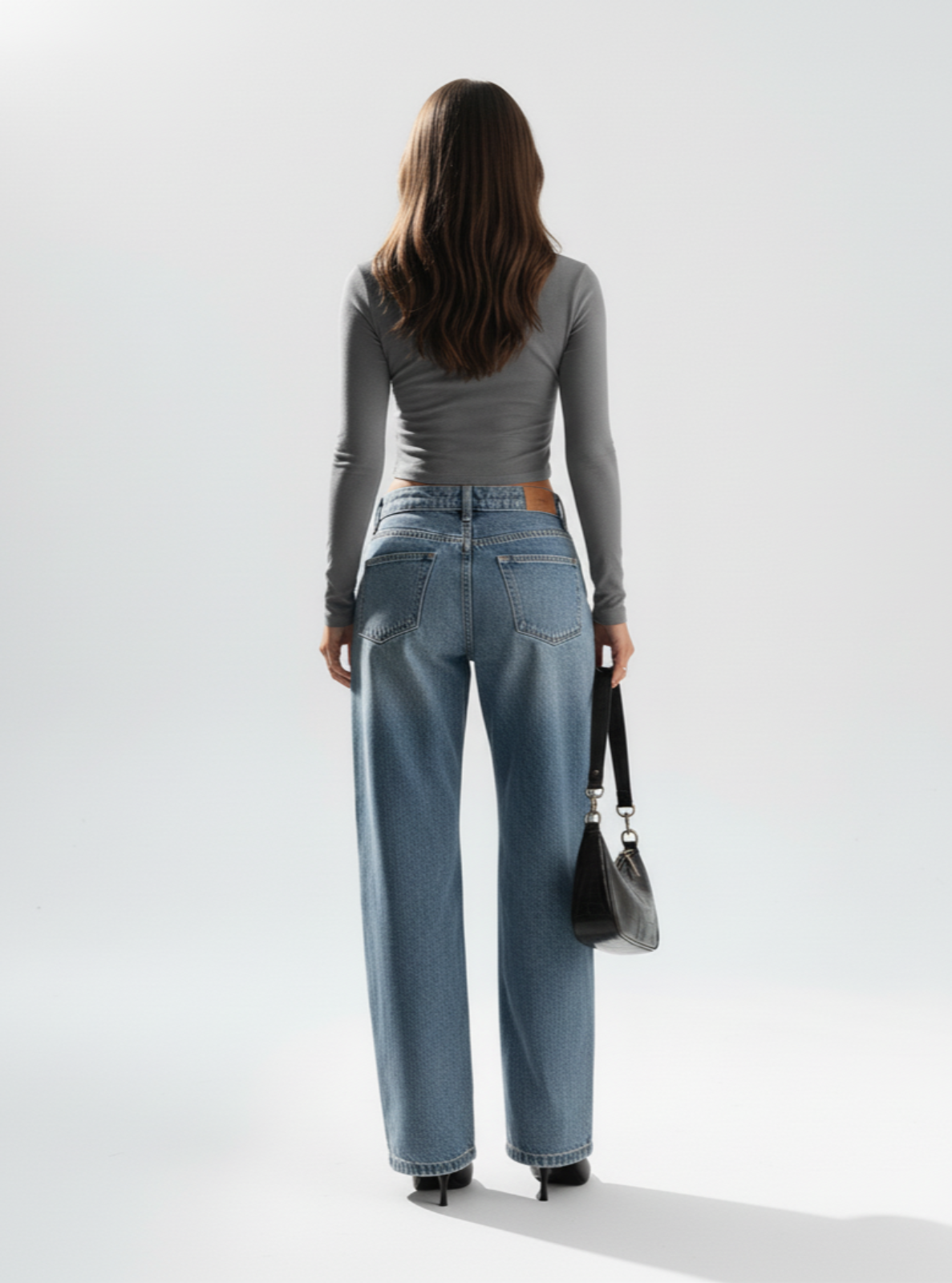 Woman wearing blue jeans and a gray top against a white background