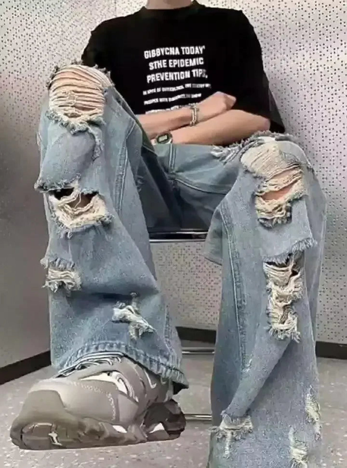 Person wearing ripped jeans and a black t-shirt with text, sitting on a chair.