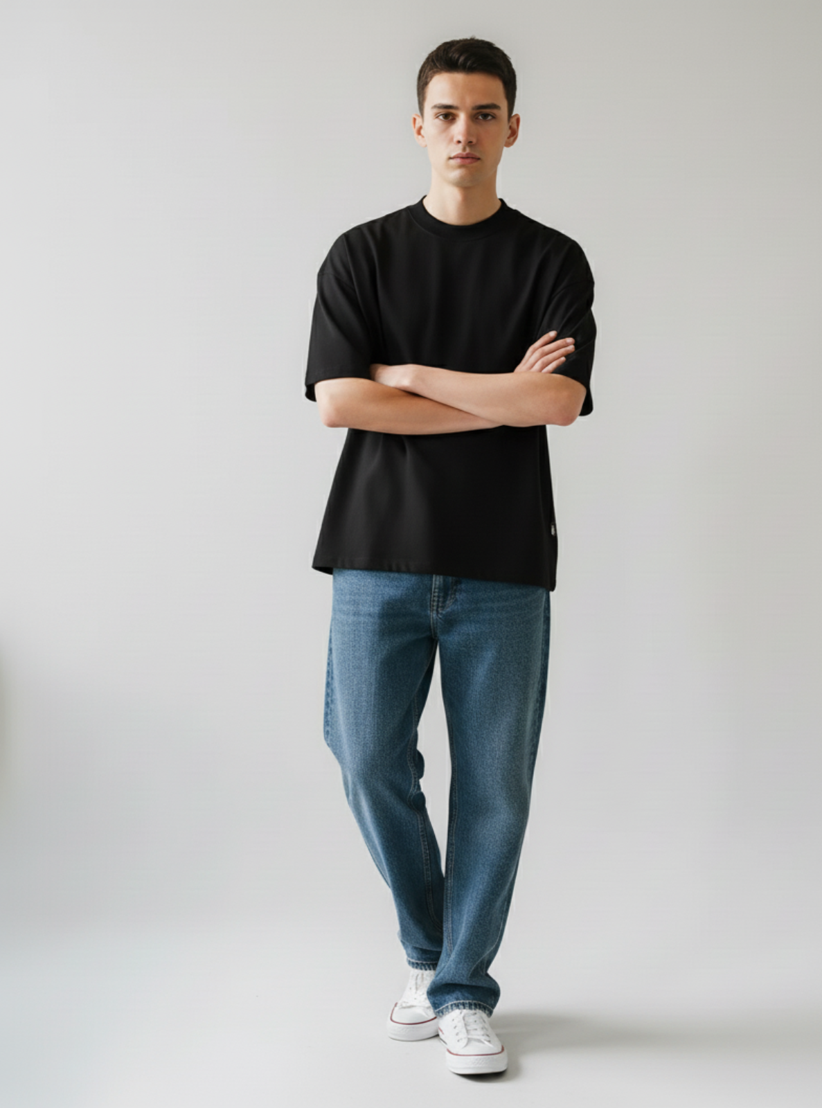 Person wearing a black t-shirt and blue jeans standing against a plain background