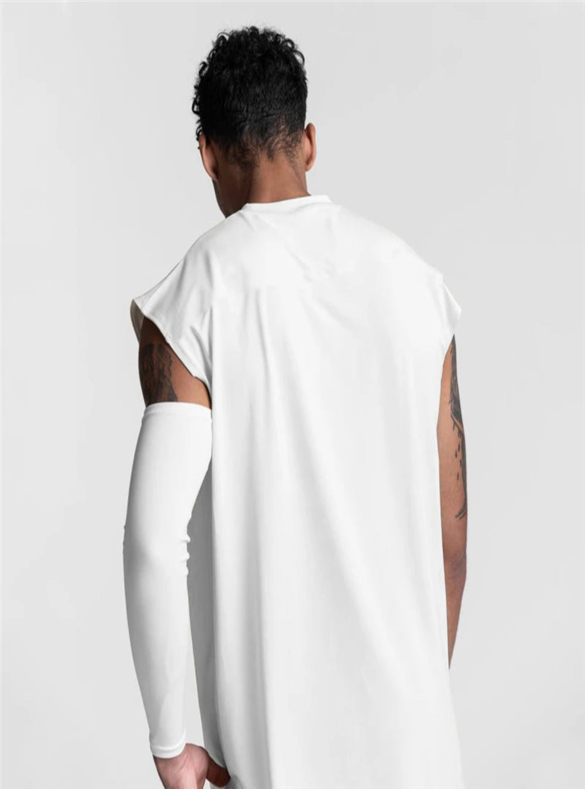 Person wearing a white t-shirt with cut-out sleeves on a plain background