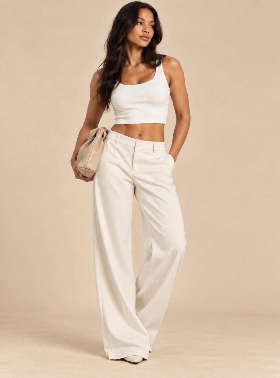 A woman modeling a white ribbed tank top and matching white wide-leg trousers, holding a beige tote bag against a solid beige studio background.