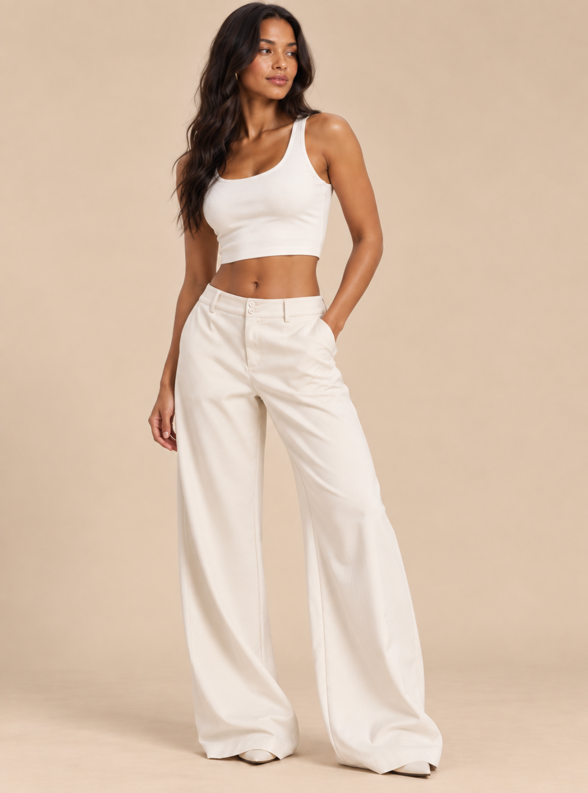 A woman modeling a white ribbed crop top and matching white wide-leg trousers against a solid beige studio background.