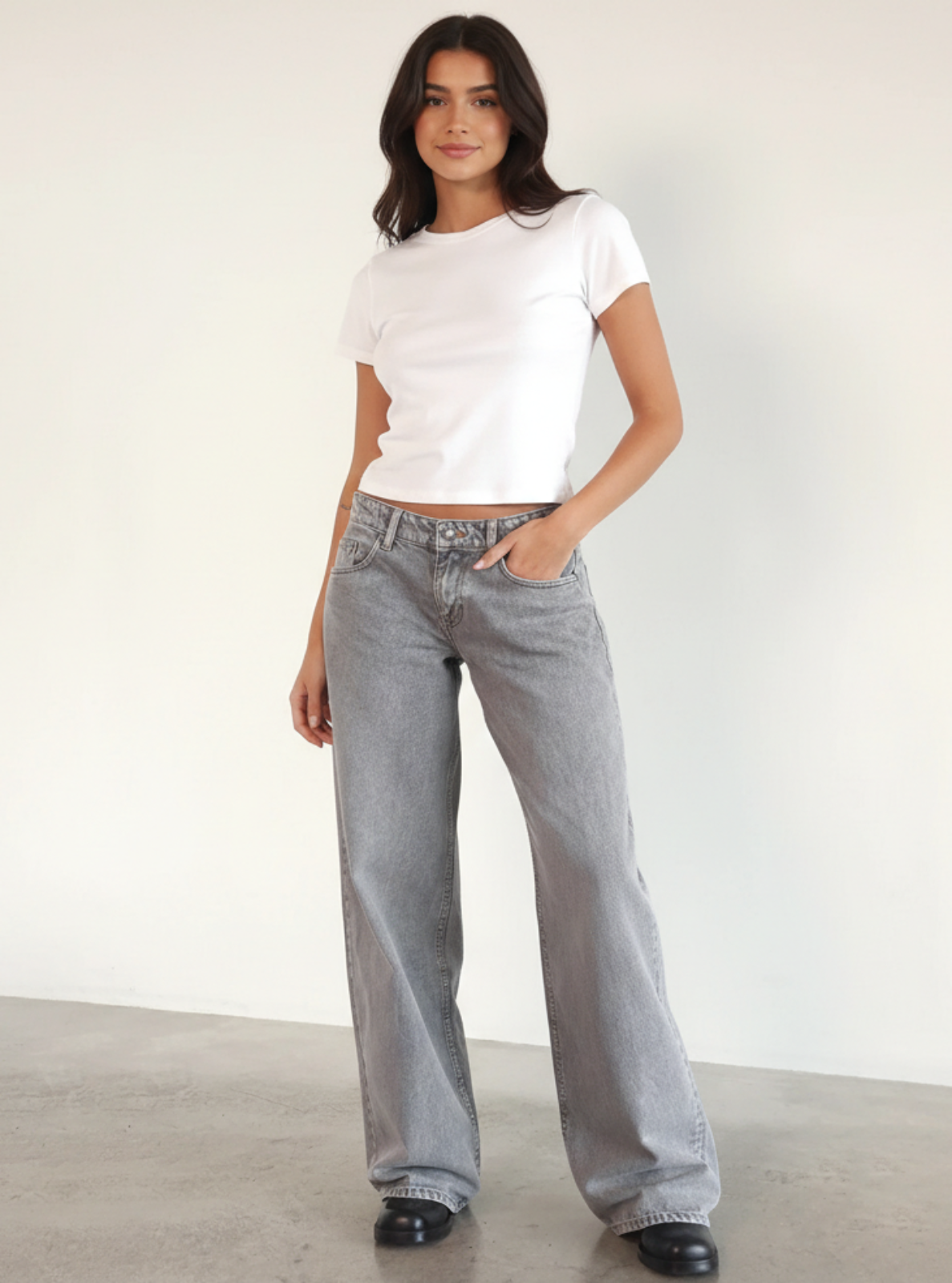 Woman wearing a white t-shirt and gray jeans against a plain background