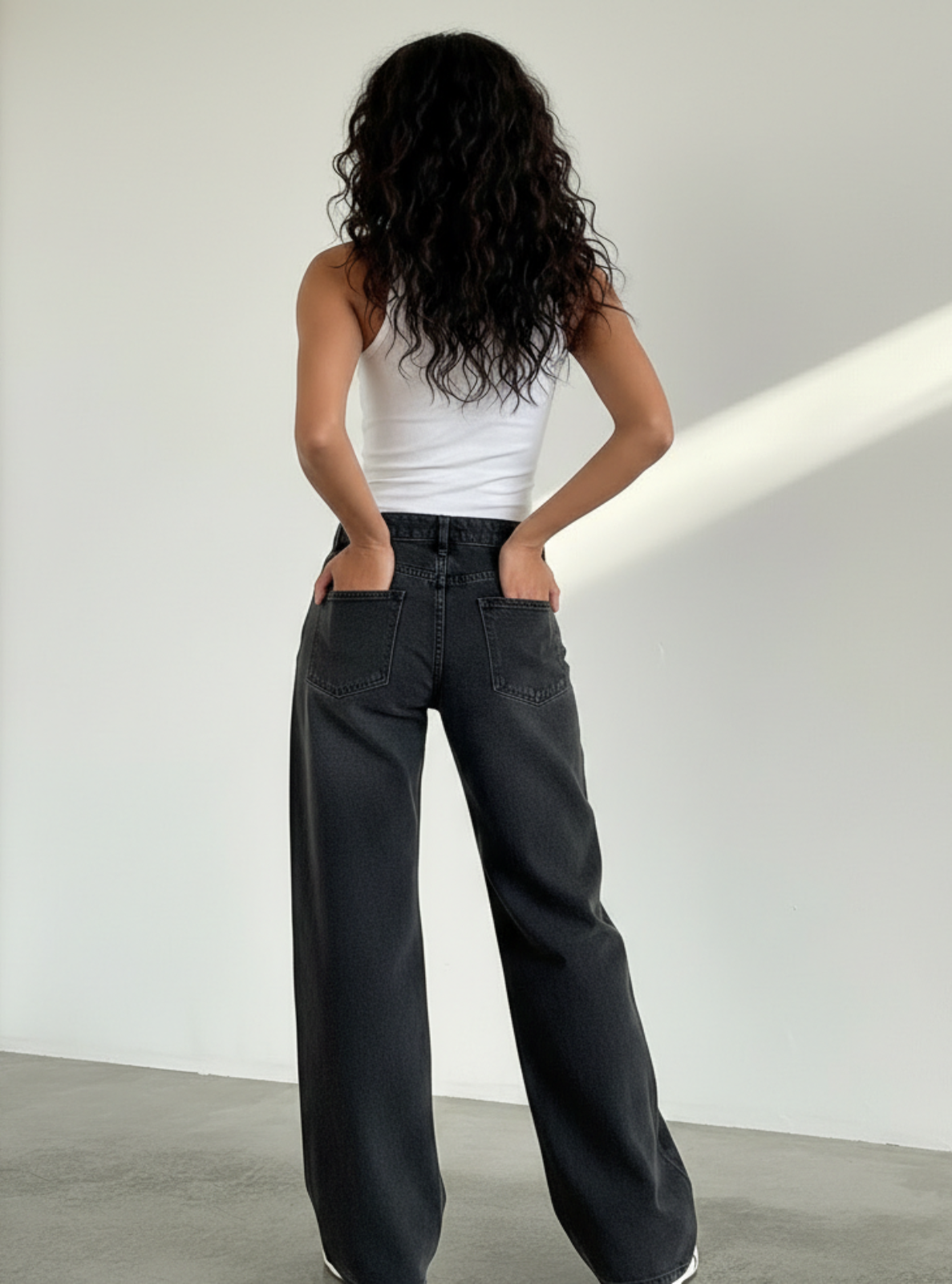 Person wearing black wide-leg jeans and a white top against a plain background