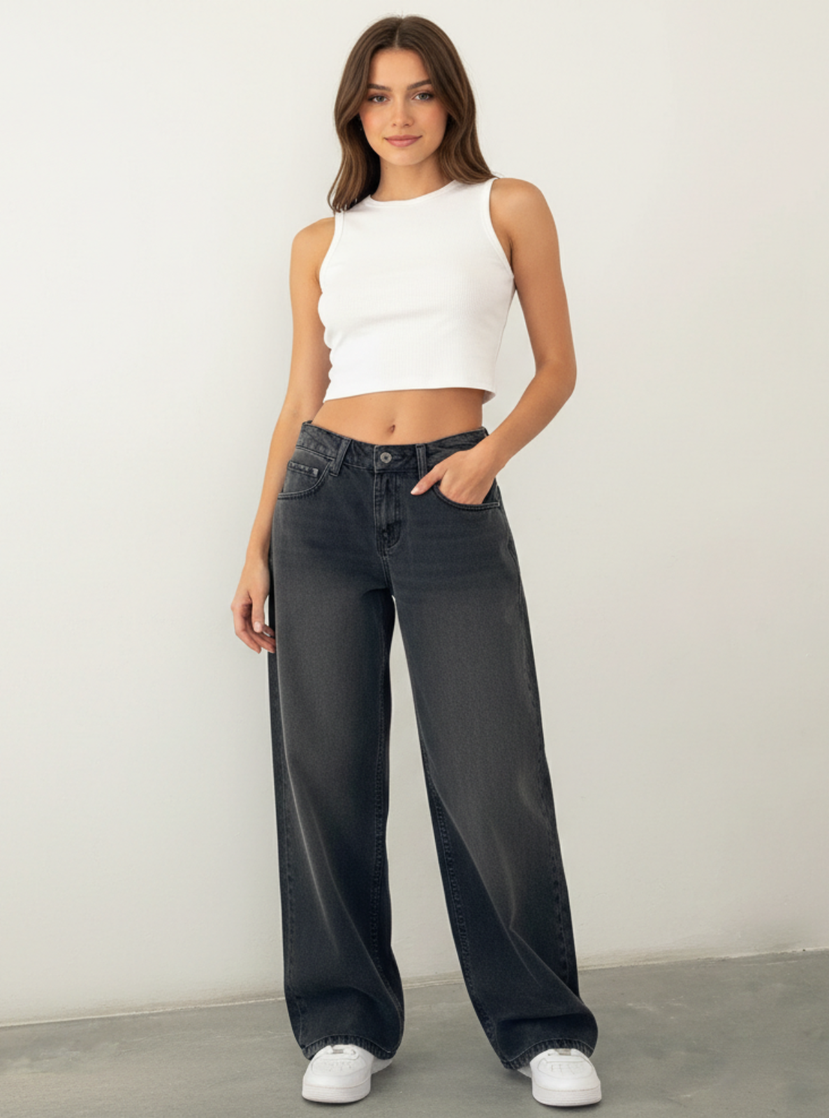 Woman wearing a white sleeveless top and black wide-leg jeans against a plain background