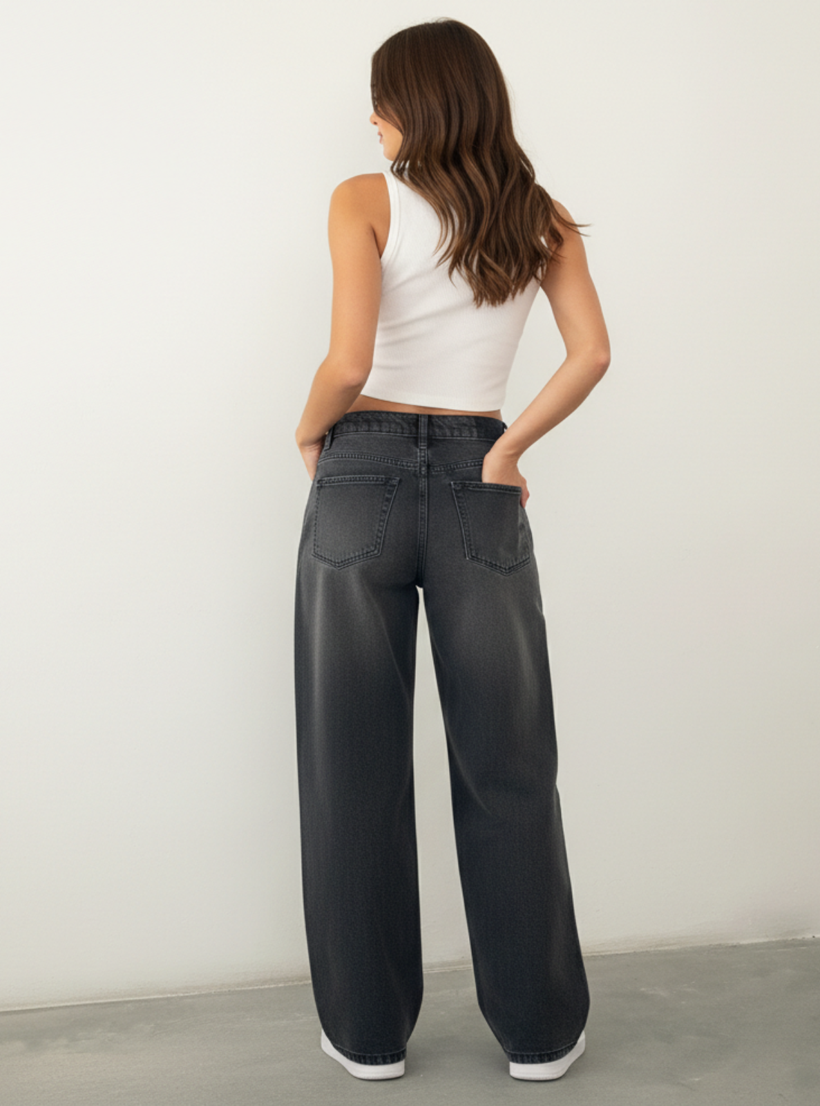 Woman wearing black jeans and a white top against a plain background